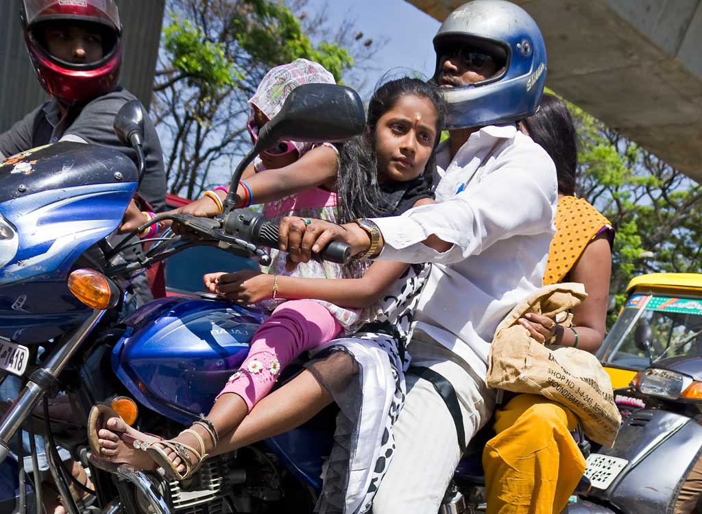 Entire family on a single motorbike. Father is driving, mother on the back and kids on the fuel tank. Although only the father wears a helmet. Taken on Mahatma Gandhi Road in Bangalore, India.