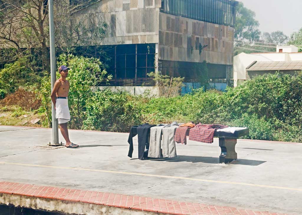 This man was washing himself and his clothes from a leaking water pipe between two rail tracks at Mysore train station in India, his clothes are laid out to dry in the sun